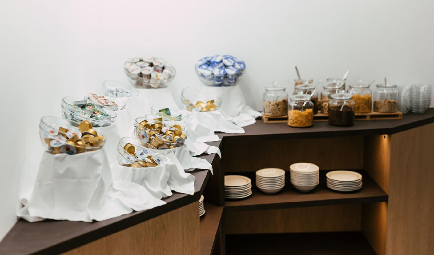 Buffet with cereals, yogurt, and plates on wooden shelves.